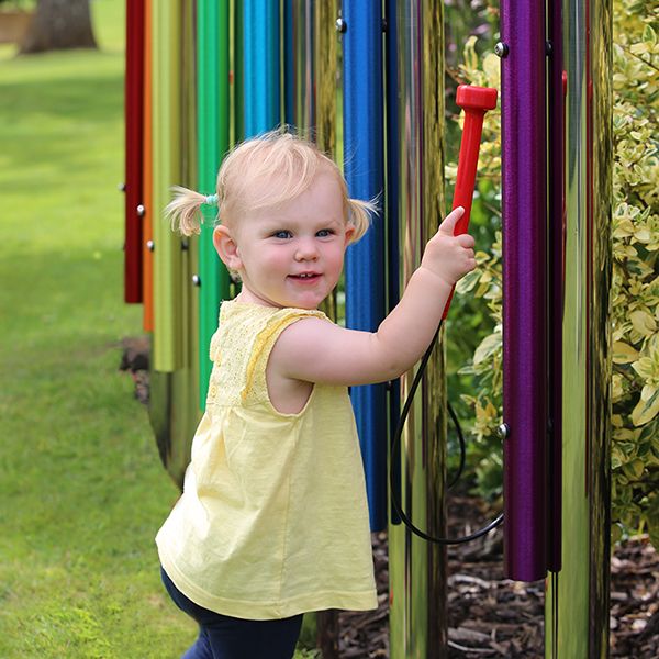 a young girl playing rainbow coloured musical chimes in a school playground