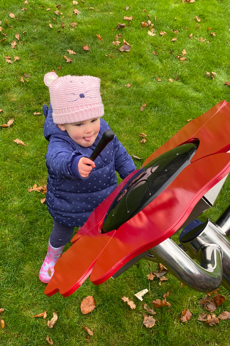 a young girl playing a red poppy shaped musical flower drum outdoors in a sensory garden