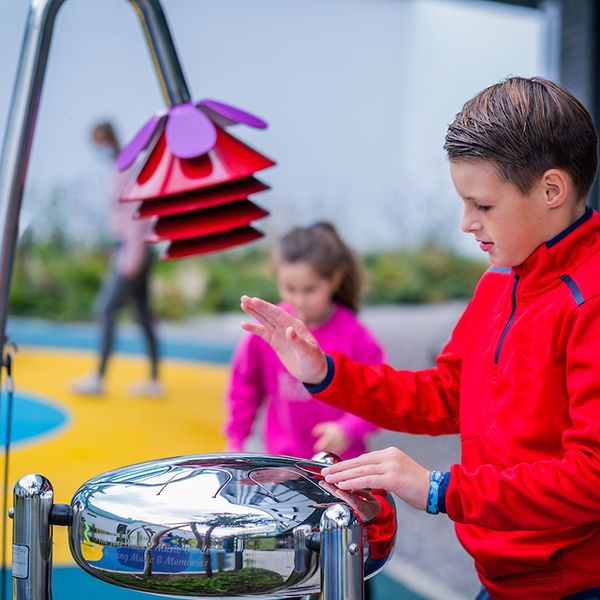 young boy in a red jumper plays an stainless steel tongue drum in the jess mackie music garden edinburgh children's hospital