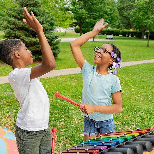 two young teens high fiving each other standing in front of an outdoor xylophone