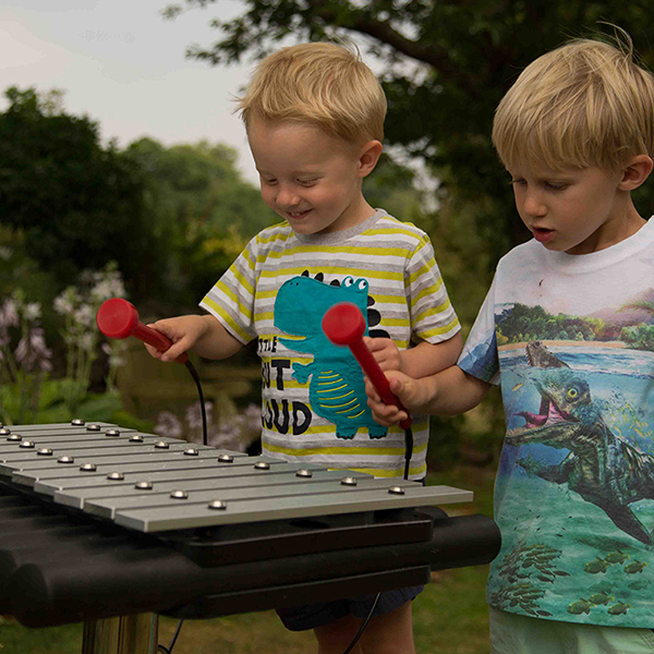 two little boys playing a silver outdoor xylophone in a garden