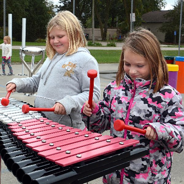 two girls playing on a large outdoor xylophone in a school playgrounds