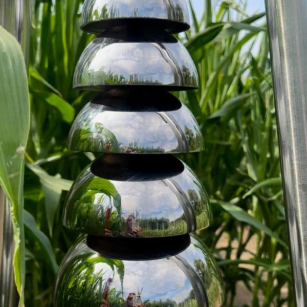 up close image of a large polished stainless steel outdoor bell lyre in a corn field