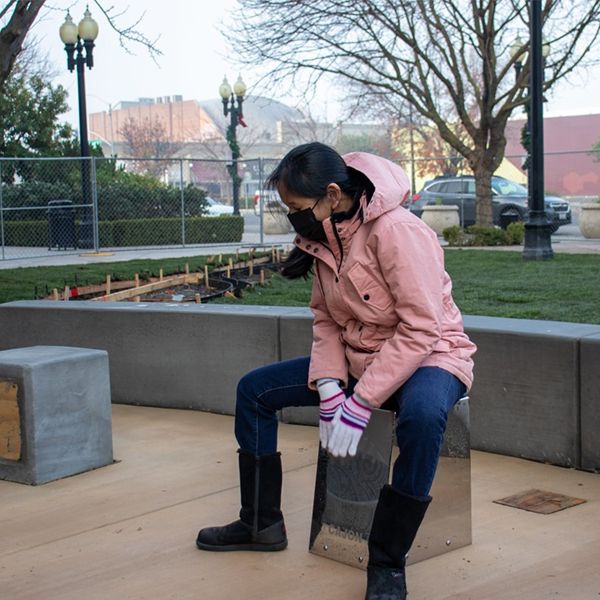 a woman wearing a face mask playing an outdoor cajon drum at the gallo center music garden