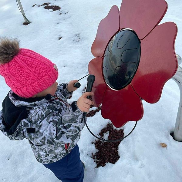 Little girl in snow gear playing an outdoor musical flower shaped like a poppy in the playground