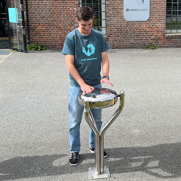 Male teenager playing an outdoor musical instrument drum outside the Vitensenteret Innlandet Science Centre in Norway