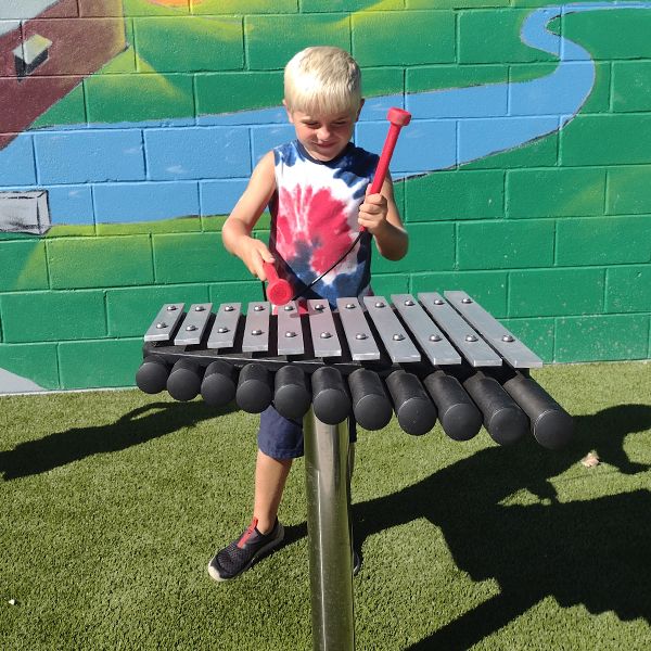 a young boy playing an outdoor xylophone with red mallets at the musical garden in town of versailles