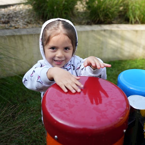 s young girl smiling and playing on a set of small outdoor drums in a museum sensory garden