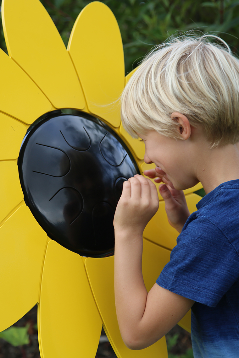 A young boy playing an outdoor musical drum in the shape and colours of a sunflower