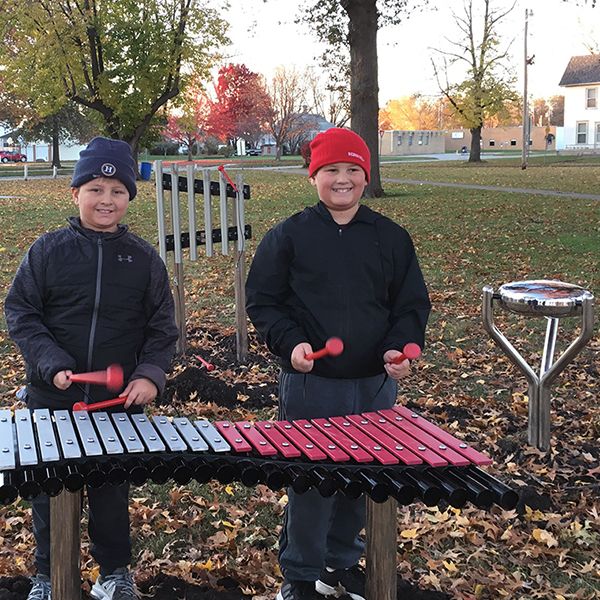 two boys wearing hats standing behind a pink and silver outdoor xylophone in Anderson Park City of Essex Iowa