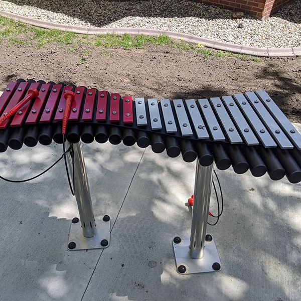 Outdoor xylophone with half pink grp notes and half aluminium notes and black resonators outside the north mankato taylor library music garden