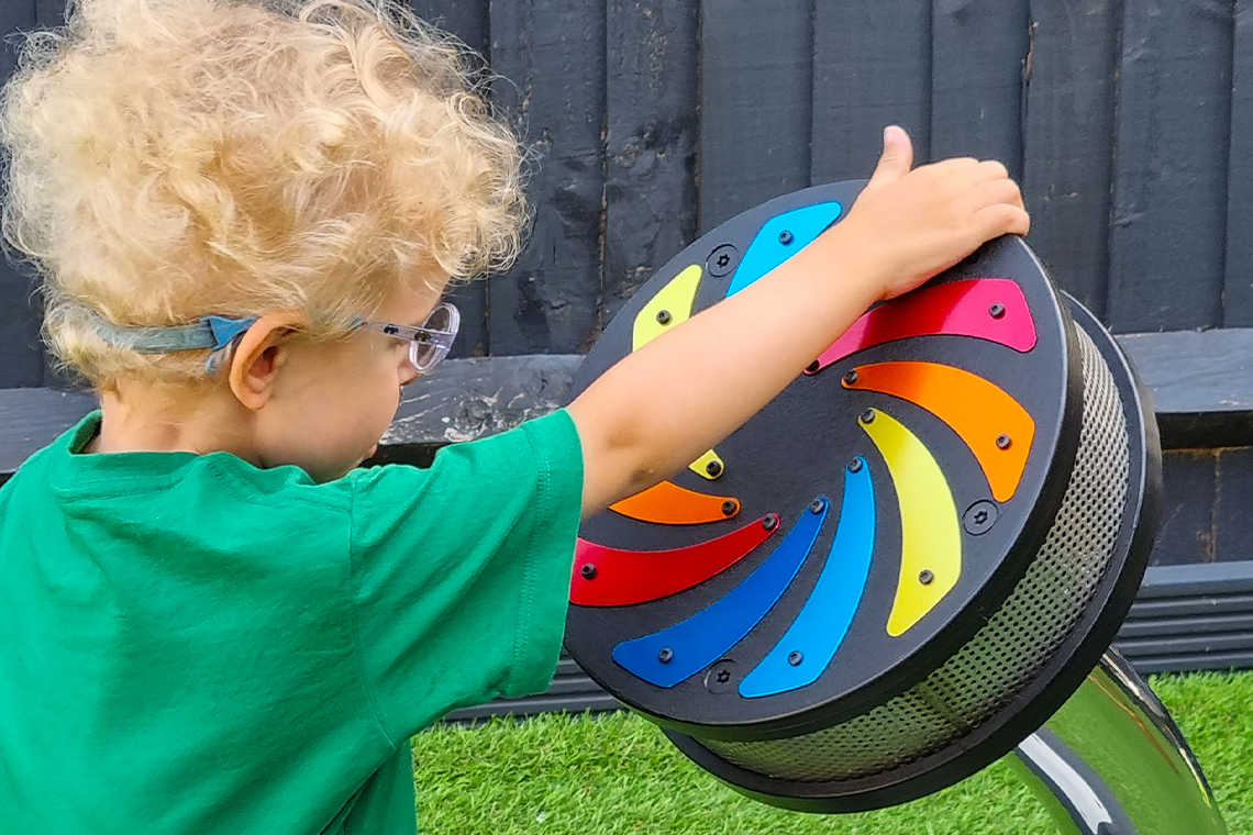 a young boy with special needs wearing a green t shirt and playing an outdoor rain wheel in the playground 