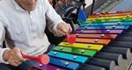 Elderley man sat playing a large colourful xylophone in a courtyard garden