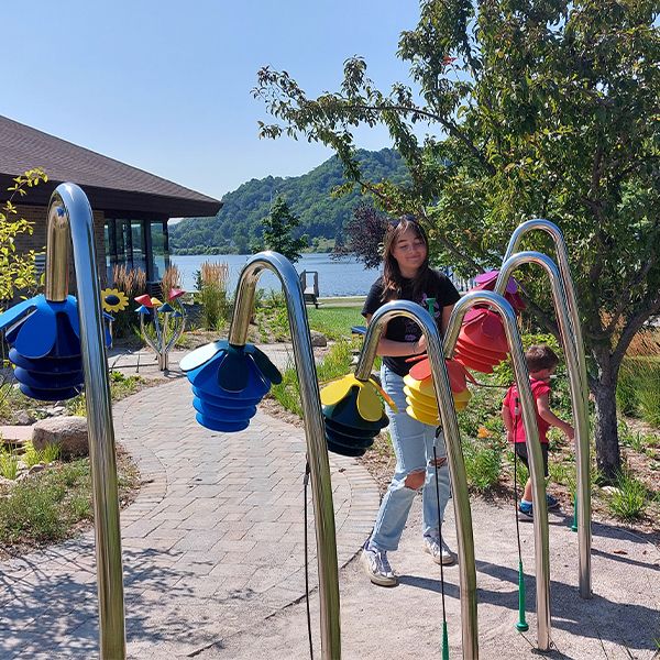 young woman playing a row of outdoor musical instruments shaped like flowers outside the Benzies Shore Library