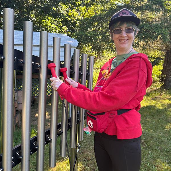 a lady wearing red playing a set of large outdoor musical chimes in the camp beausite new music garden