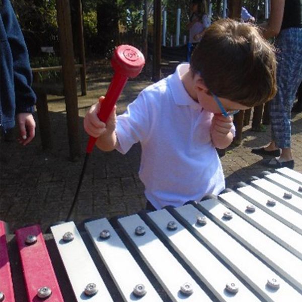 child with special needs playing an outdoor xylophone with pink and silver notes