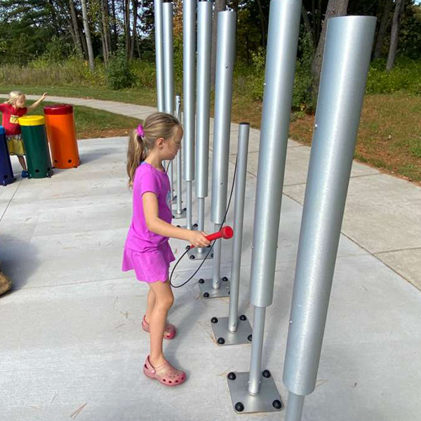a young girl playing large silver outdoor musical chimes in a play park