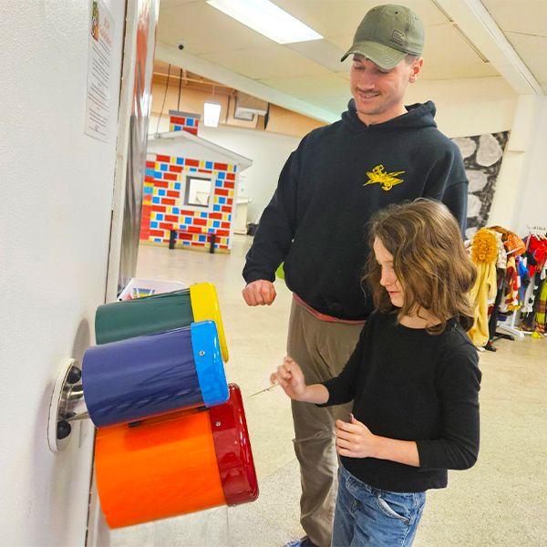 a father and daughter playing a set of three colourful bongo drums attached to a wall in the baraboo childrens museum