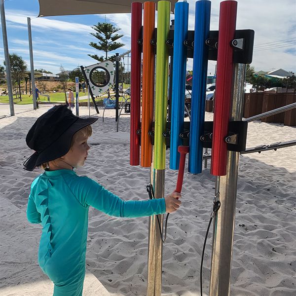 a young boy in swim wear playing a outdoor musical chimes in a playground on the beach