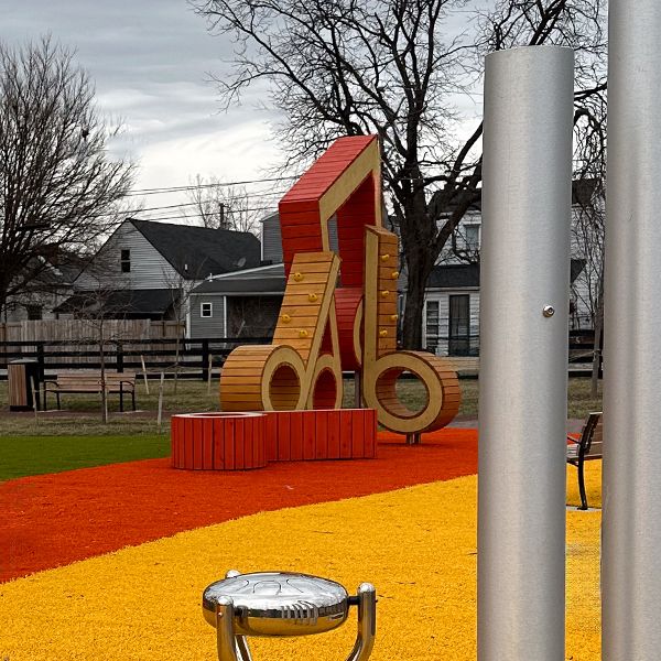 a wooden playground climbing structure with large wooden musical notes attached in a playground