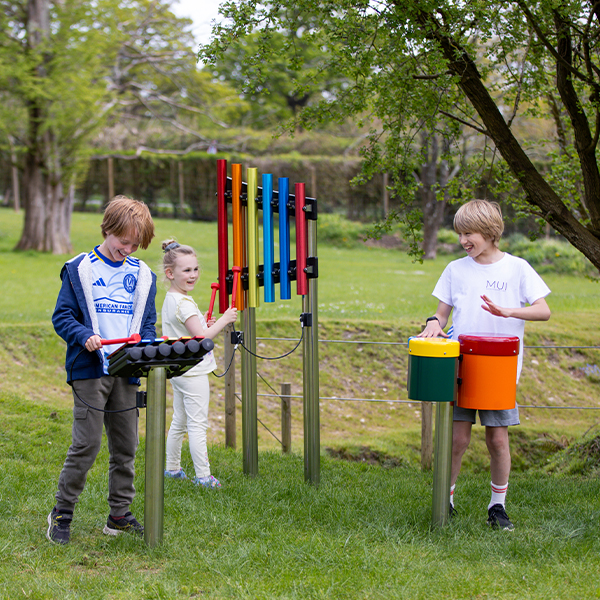 Three children in a park laughing while playing rainbow coloured outdoor musical instruments