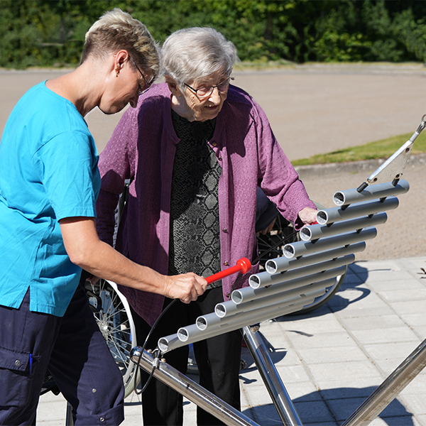 A senior lady and her carer playing a metallophone with red mallets in a senior living music courtyard