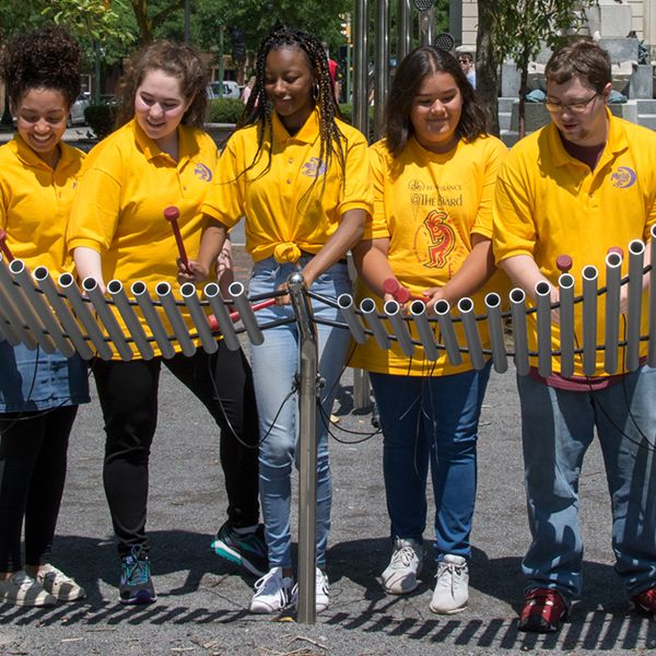 Five Teenagers dressed in yellow t-shirts playing an outdoor musical instrument in Syracuse USA