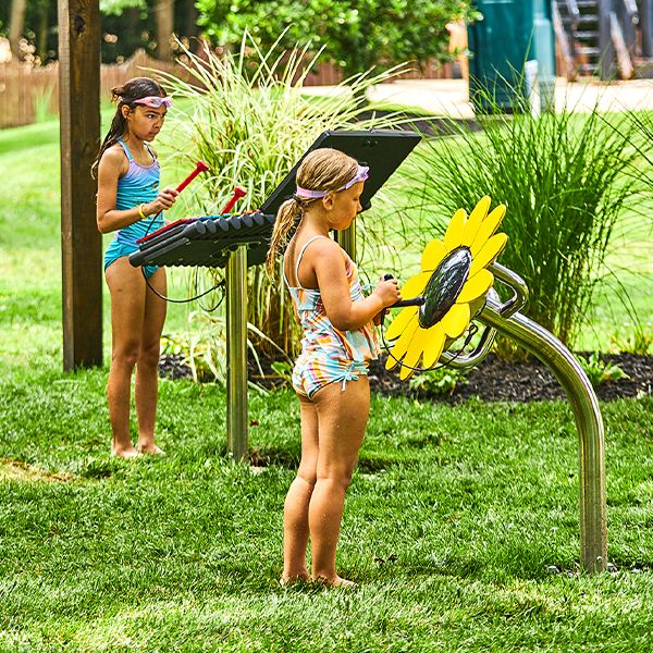 two girls in swimming costumes playing outdoor musical instruments in the Chartwell Happy Day Camp musical garden