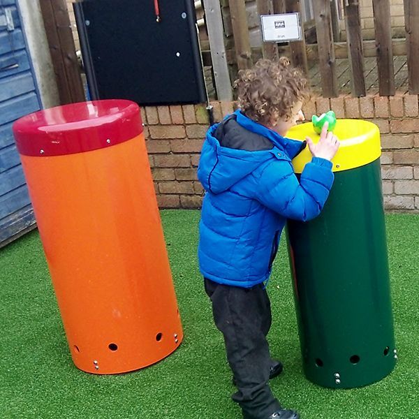 young boy standing hitting large outdoor drum with his hands in special needs school playground