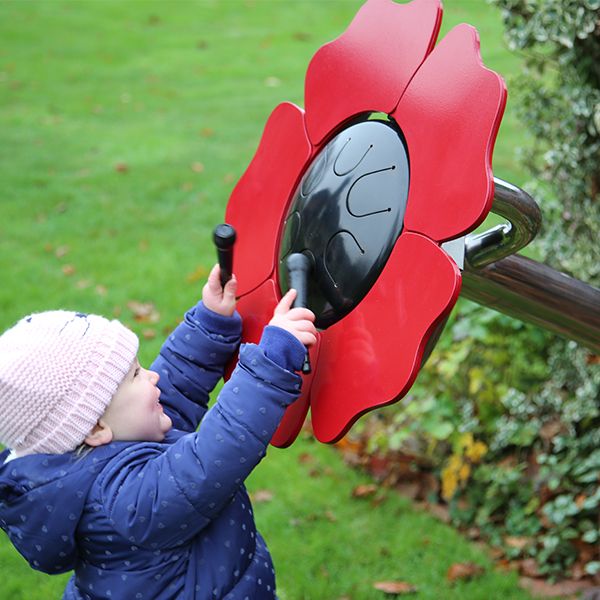 a young girl playing a red poppy shaped musical flower drum outdoors in a sensory garden