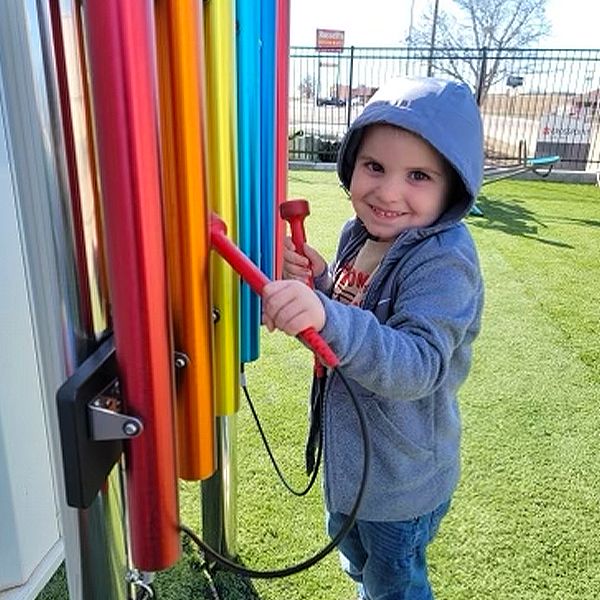 A young boy playing a set of outdoor rainbow chimes in cross church preschool music garden