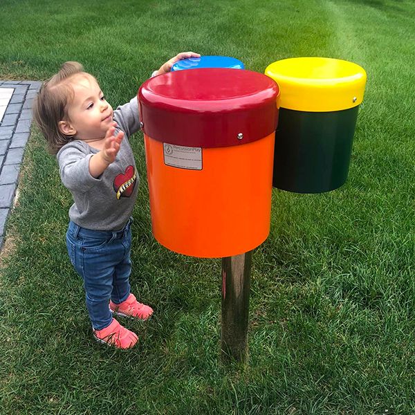 image of a small child reaching up and playing a set of three outdoor drums on a post