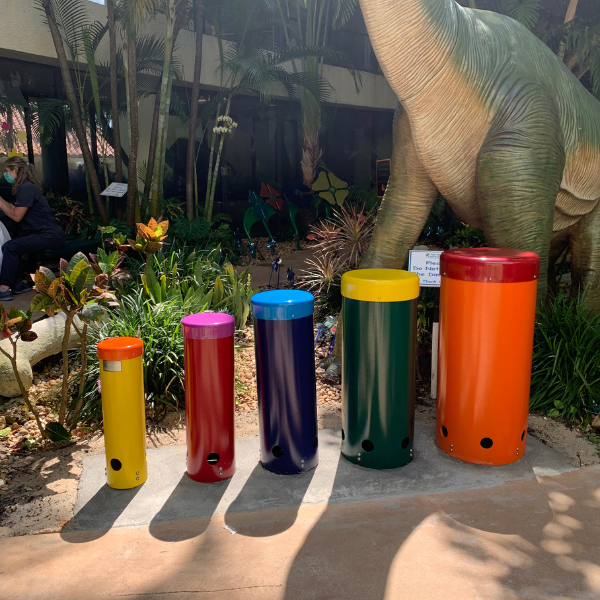 five brightly colored drums installed in a healing garden in front of a giant dinosaur sculpture