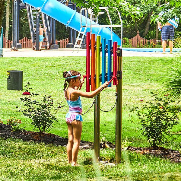 a young girl wearing a swimming costume playing large colourful outdoor musical chimes