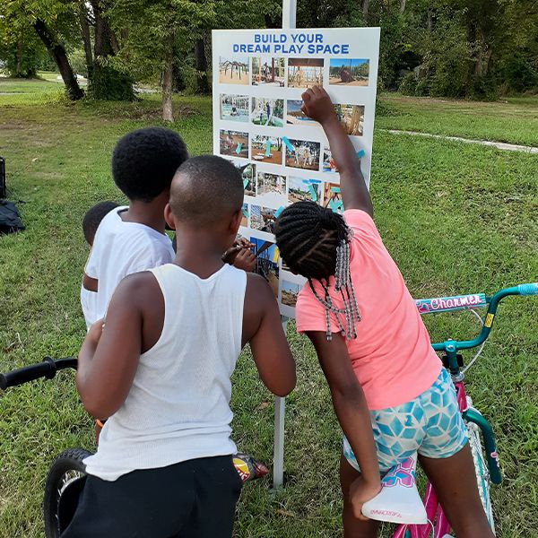 the back of three children looking at a poster of a new playground proposal pinned to a post 