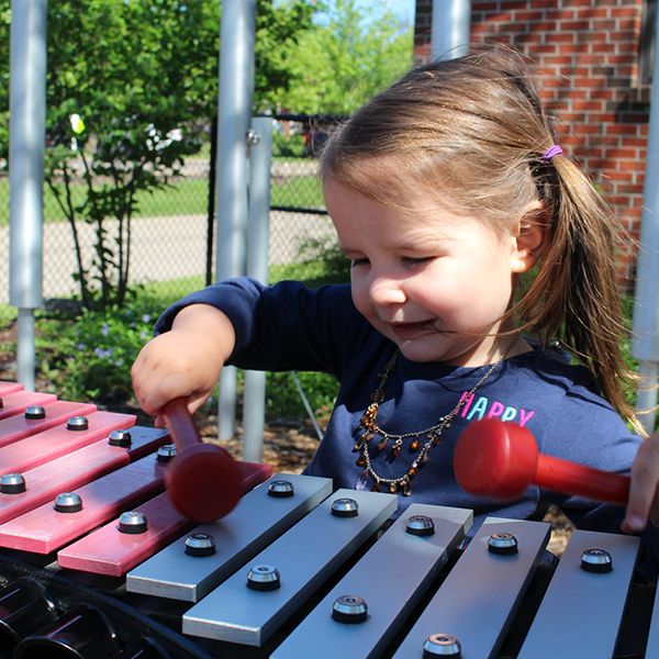 a close up of a little girl playing on the outdoor xylophone at the children's healing center