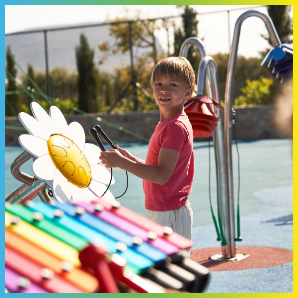 boy playing an outdoor drum shaped like a daisy with a xylophone in the foreground and outdoor musical flowers in the background