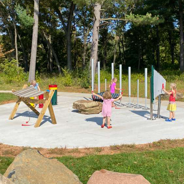 a group of young girls playing on a selection of outdoor musical instruments  in a park